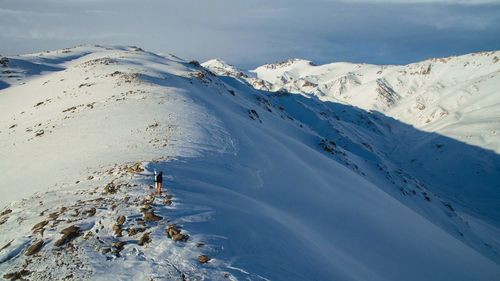 Hiker standing on snowcapped mountain peak against sky