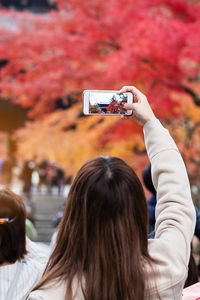 Rear view of woman photographing autumn tree