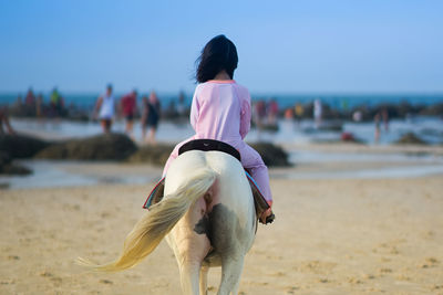 Rear view of girl riding horse on beach