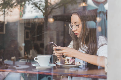 Woman with cake checking her cell phone in a cafe