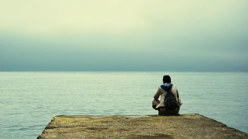 Rear view of man sitting on shore against sea