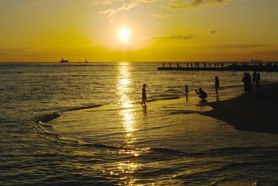 Silhouette people on sea against sky during sunset