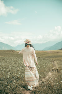 Rear view of woman walking on footpath amidst field against sky