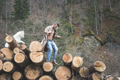 Young man with dog on logs of wood in forest