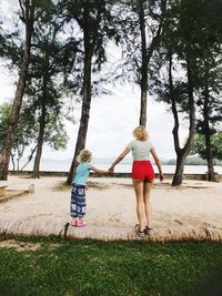 Rear view of mother and daughter walking on tree trunk