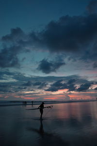 Silhouette people on beach against sky during sunset