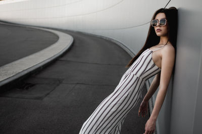 Portrait of woman wearing sunglasses while leaning on wall