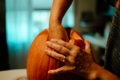 Midsection of person carving pumpkin on table at home