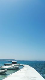 Boats moored in sea by pier against clear blue sky