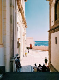 People on steps amidst buildings by sea