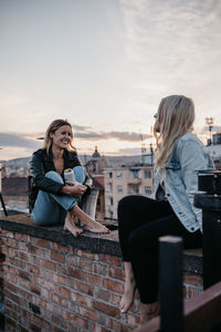 Woman sitting in city against sky during sunset