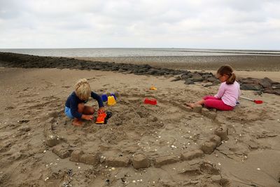 Side view of boy and girl sitting on sand at beach