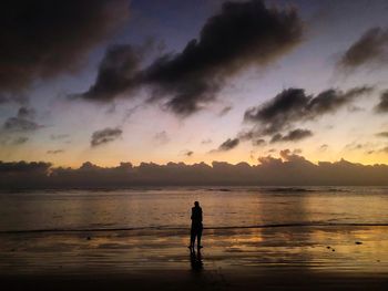 Silhouette woman standing on beach against sky during sunset