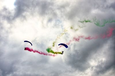 Low angle view of vapor trails and paragliders against cloudy sky