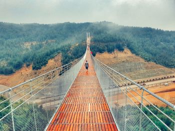 Rear view of man walking on footbridge against mountains