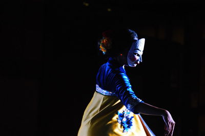 Side view of woman dancing while wearing mask at night