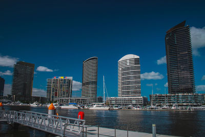 Modern buildings by river against blue sky in city