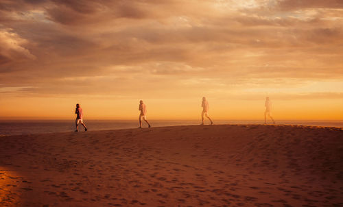 Multi exposure on man walking at beach against cloudy sky during sunset