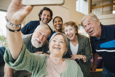 Senior woman taking selfie with friends and healthcare workers at retirement home