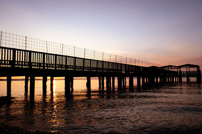 Silhouette pier over sea against sky during sunset