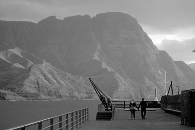 Rear view of couple walking on promenade by sea and mountain