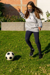 Full length of woman in mask playing with soccer ball at lawn