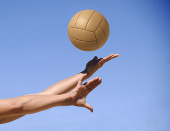 Cropped hands of woman playing with ball against clear blue sky during sunny day