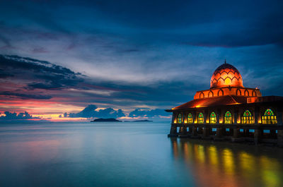 Illuminated mosque by sea at dusk