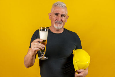 Portrait of young man drinking bottle against yellow background