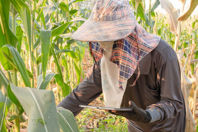 Side view of farmer with digital tablet examining crops at farm