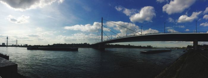 View of suspension bridge over river against cloudy sky
