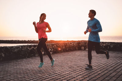 Full length of friends running at beach against sky during sunset