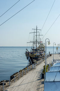 Sailboats moored on pier by sea against clear sky