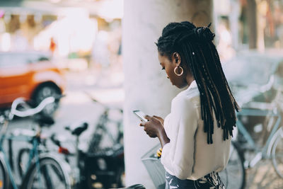 Young woman using smart phone while standing on footpath in city