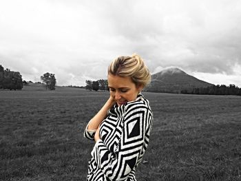 Smiling young woman standing on grassy field against cloudy sky