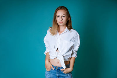 Young woman posing in white shirt and jeans on blue background