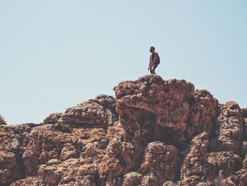 Low angle view of man standing on rock against clear sky