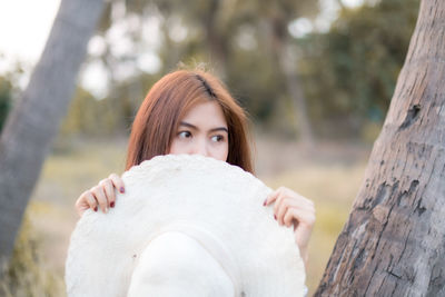 Portrait of young woman against tree trunk