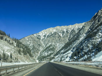 Road amidst snowcapped mountains against clear blue sky