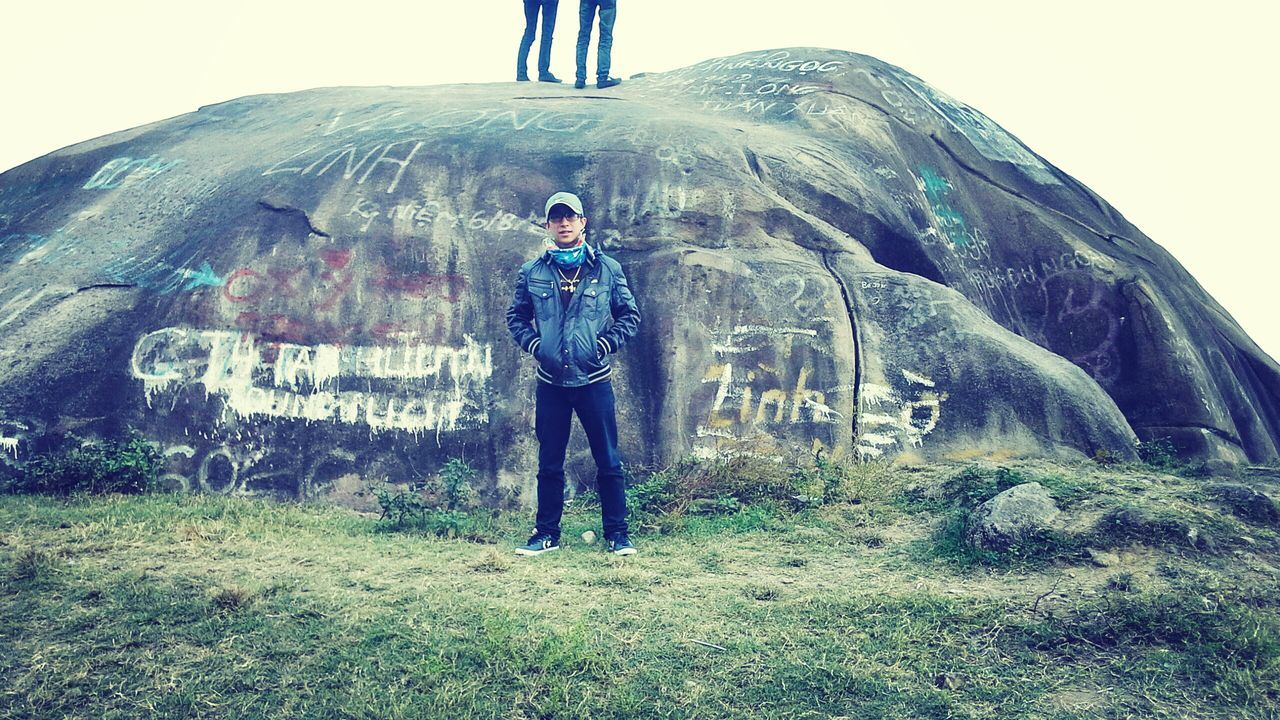 lifestyles, full length, leisure activity, casual clothing, mountain, standing, men, young men, rock - object, low angle view, sky, young adult, clear sky, day, nature, front view, grass, hiking