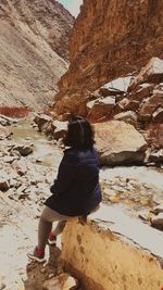 Rear view of woman sitting on rock formation against sky