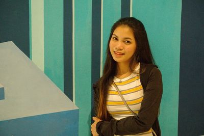 Portrait of young woman smiling while standing against wall