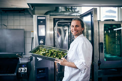 Portrait of confident chef with broccoli in baking sheet at commercial kitchen