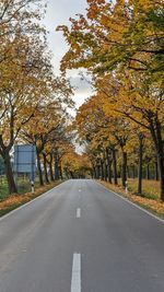 Empty road amidst trees against sky during autumn