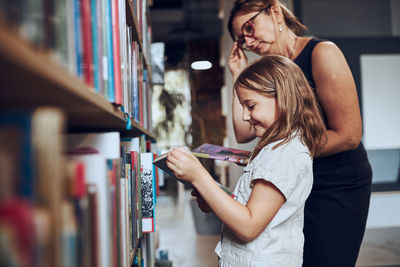 Teacher helping to choose book her schoolgirl in school library. smart girl selecting literature