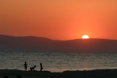 Silhouette people by sea against sky during sunset