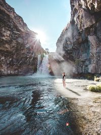 Woman standing in river against waterfall in sunny day