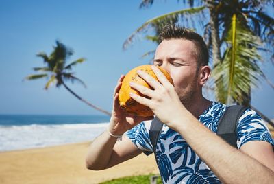 Man drinking coconut at beach against sky