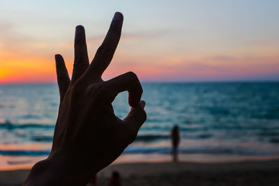 Close-up of hand against sea during sunset