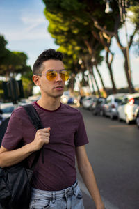 Young man wearing sunglasses standing against car
